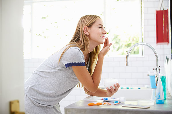woman putting on moisturizer in bathroom